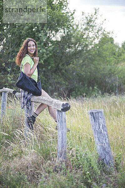 Junge Frau sitzt auf einem beschädigten Holzzaun in einem Feld