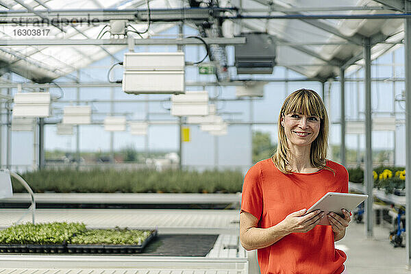 Lächelnde Unternehmerin  die ein digitales Tablet benutzt  während sie in einer Gärtnerei steht
