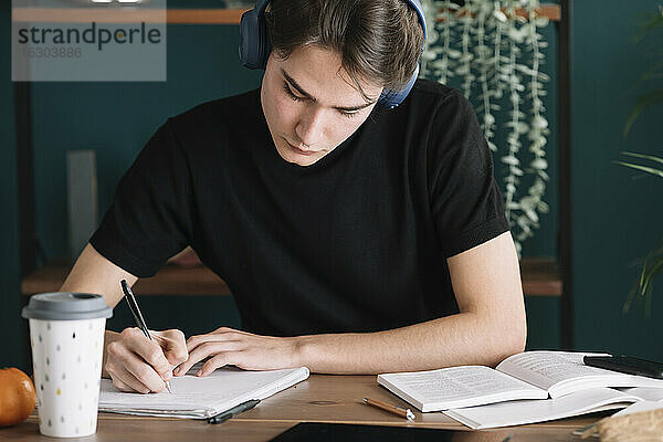 Mann schreibt in ein Buch  während er zu Hause über Kopfhörer Musik hört