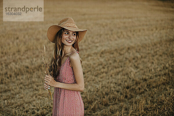 Frau blickt über die Schulter  während sie die Weizenernte auf einem Bauernhof hält