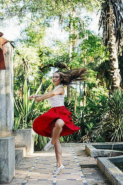 Junge Frau mit langen Haaren tanzt auf dem Fußweg gegen Bäume im Park