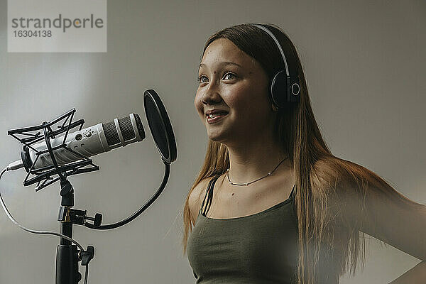 Nahaufnahme eines lächelnden Teenagers  der über ein Mikrofon an der Wand eines Aufnahmestudios singt