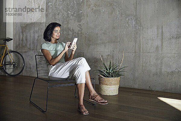 Geschäftsfrau  die ein Smartphone benutzt  während sie auf einem Stuhl an der Wand im Büro sitzt