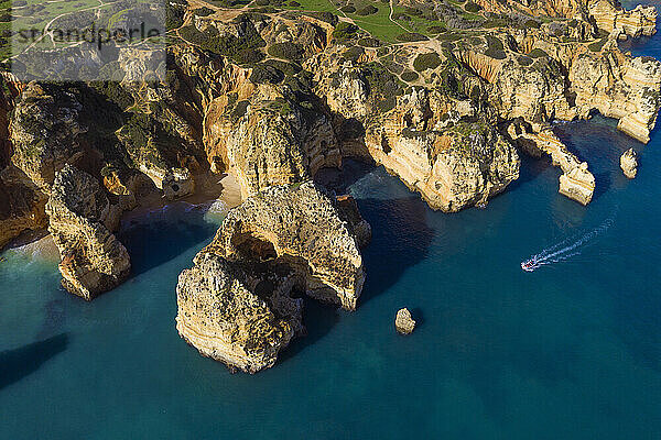 Portugal  Algarve  Lagos  Drohnenansicht eines Motorboots  das sich auf die Schornsteine der Landzunge Ponta da Piedade zubewegt