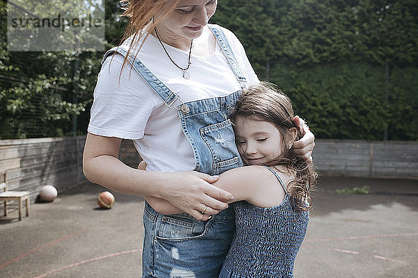 Tochter umarmt Mutter auf Basketballplatz im Hinterhof