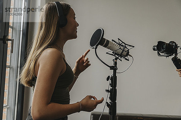 Teenager-Mädchen mit Kopfhörern singt über Mikrofon im Studio