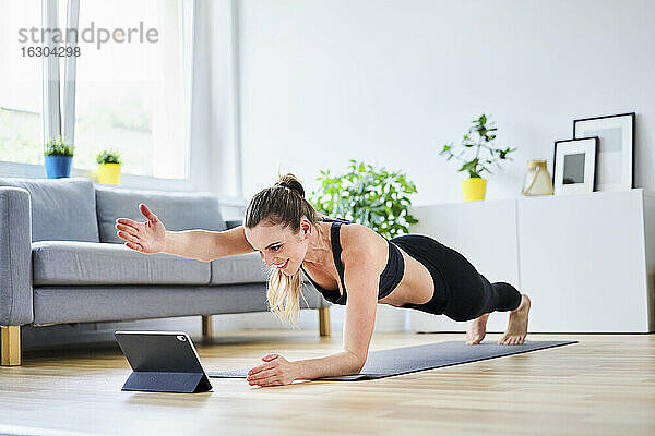 Frau streckt den Arm während der Plank-Pose aus  während sie im Internet über einen Tablet-PC eine Übung lernt