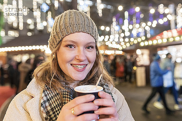 Nahaufnahme einer glücklichen schönen Frau mit heißer Schokolade auf einem nächtlichen Weihnachtsmarkt