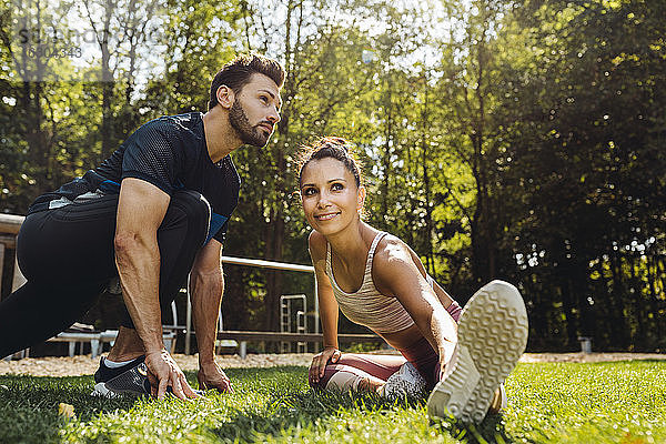 Mann und Frau dehnen sich im Gras in der Nähe eines Fitnessparcours