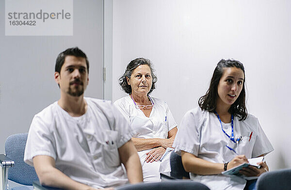 Ärzte hören in einer Sitzung zu  während sie im Krankenhaus an der Wand sitzen