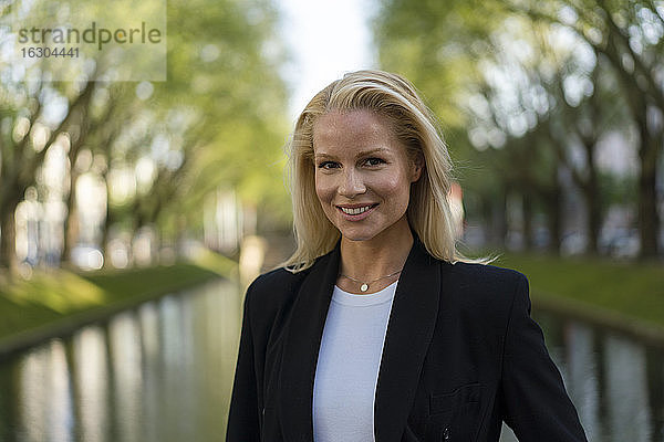 Lächelnd schöne blonde Unternehmerin stehend gegen Kanal in der Stadt