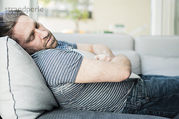 Mann mit Laptop schlafend auf Sofa im Wohnzimmer