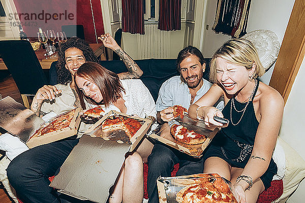 Fröhliche Freunde sehen fern  während sie auf einer Party zu Hause Pizza essen