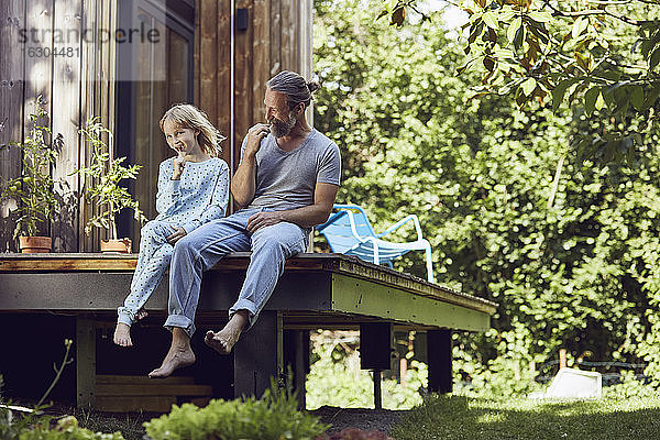 Vater und Tochter putzen sich die Zähne  während sie vor einem kleinen Haus sitzen
