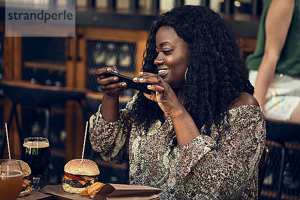 Lächelnde Frau mit Smartphone beim Burgeressen in einer Kneipe