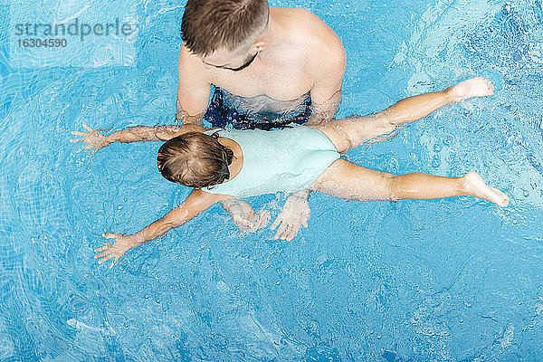 Kleines Mädchen  das mit seinem Onkel im Schwimmbad schwimmen lernt
