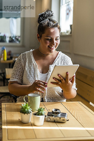 Lächelnde junge Frau  die ein digitales Tablet benutzt  während sie an einem Tisch in einem Café sitzt