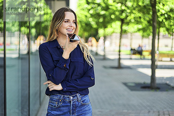 Lächelnde Frau  die den Blick abwendet  während sie über ihr Smartphone spricht