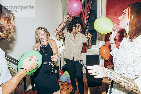 Freunde tanzen mit Luftballons während einer Party zu Hause