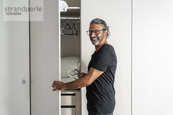 Lächelnder Mann ordnet Kleiderbügel im Kleiderschrank zu Hause