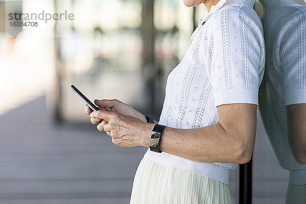 Nahaufnahme einer Frau  die sich beim Benutzen eines Smartphones in der Stadt anlehnt