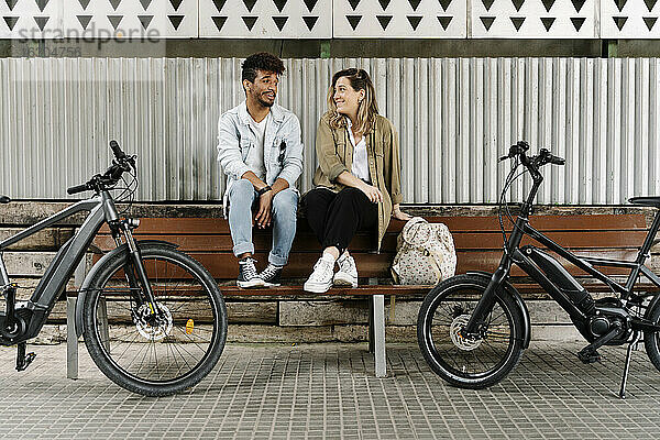 Paar sitzt auf einer Bank  während Elektrofahrräder auf dem Fußweg geparkt sind