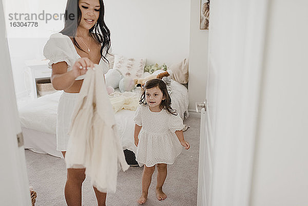 Lächelnde Mutter hält das Kleid ihrer Tochter im Schlafzimmer