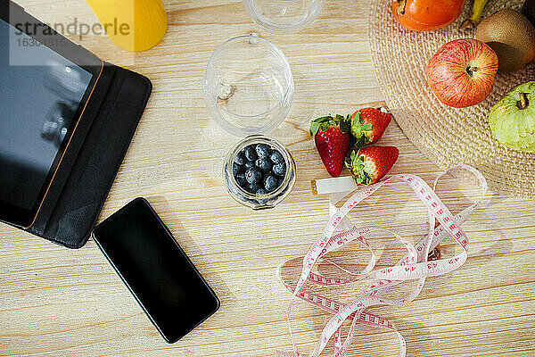 Digitales Tablet und Mobiltelefon mit Obst und Maßband auf dem Tisch zu Hause