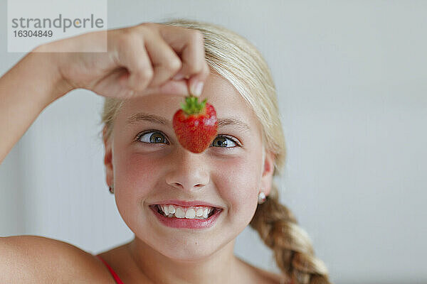 Lächelndes blondes Mädchen mit Blick auf eine Erdbeere