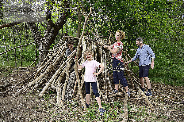 Familie lächelt beim Bau eines Lagers mit Baumstämmen im Wald