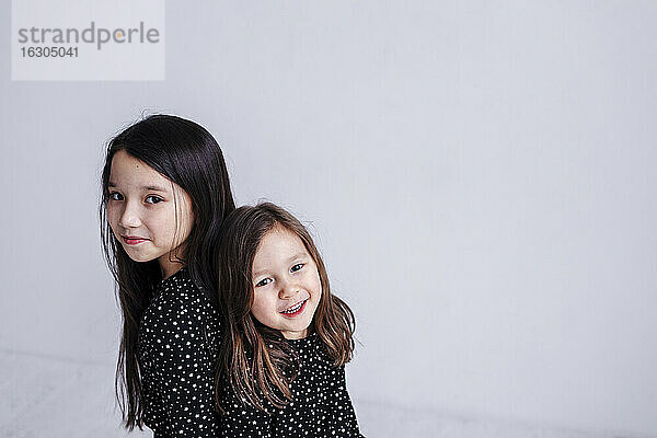 Cute Schwestern stehen Rücken an Rücken gegen weißen Hintergrund im Studio