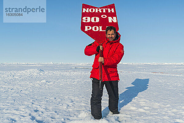 Porträt eines Mannes  der mit einem Schild am Nordpol posiert