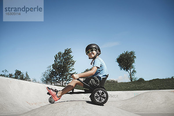 Kleiner Junge sitzt auf dem Hoverboard im Skateboard-Park an einem sonnigen Tag