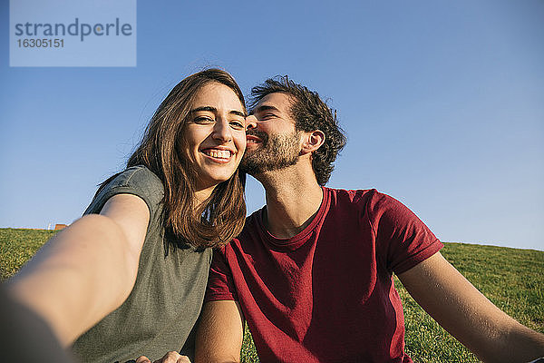 Frau  die ein Selfie mit einem Mann macht  während sie im Gras sitzt