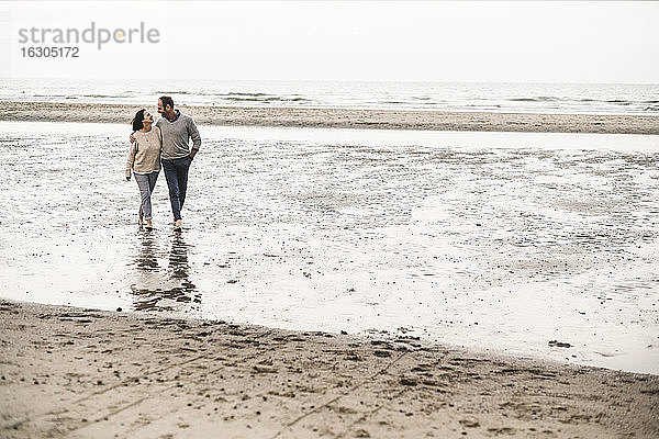 Romantisches Paar spaziert am Strand gegen den Himmel bei Sonnenuntergang