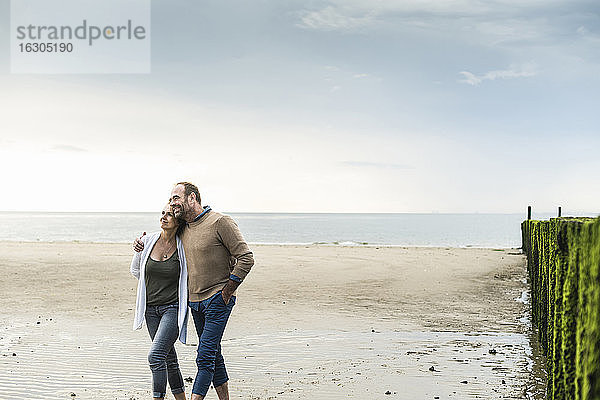 Verliebtes reifes Paar spaziert am Strand gegen das Meer bei Sonnenuntergang