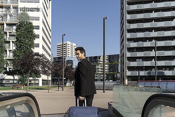 Geschäftsmann mit Koffer zu Fuß auf dem Gehweg gegen den klaren Himmel in der Stadt