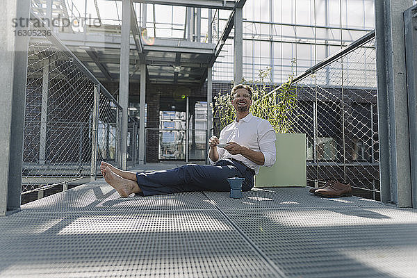 Lächelnder Geschäftsmann mit Kaffee auf dem Boden sitzend in einer Gärtnerei
