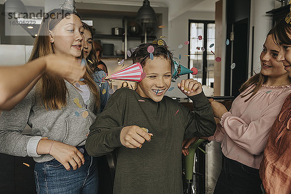 Fröhlicher Junge mit Partyhüten  der sich mit Freunden auf einer Geburtstagsfeier zu Hause amüsiert