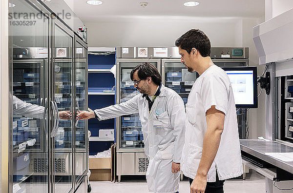 Arzt steht mit männlichem Mitarbeiter und öffnet Kühlschrank in Apotheke