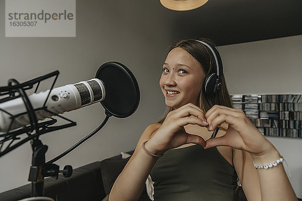 Lächelndes Teenager-Mädchen  das beim Singen im Aufnahmestudio ein Herz formt