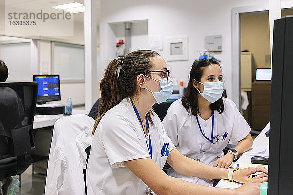 Pharmazeutinnen mit Masken  die im Krankenhaus sitzend am Computer diskutieren