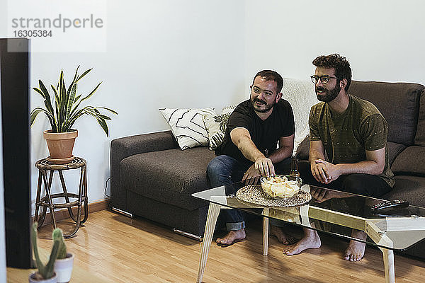 Männliche Freunde schauen Sport im Fernsehen  während sie auf dem Sofa im Wohnzimmer sitzen