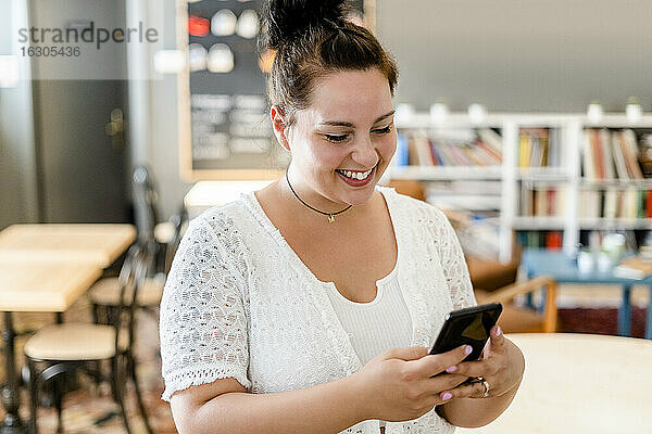 Glückliche junge Frau  die in einem Café steht und ihr Smartphone benutzt