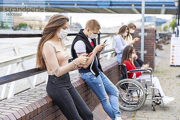Junge Freunde halten bei der Benutzung von Handys in der Stadt einen Sicherheitsabstand ein