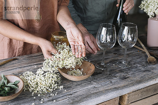 Mittelteil eines Paares bei der Zubereitung eines frischen Cocktails mit weißen Blumen auf einem Holztisch