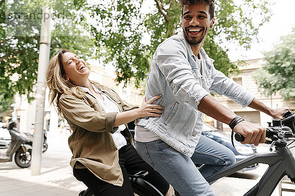 Fröhliches junges Paar genießt Fahrt auf elektrischem Fahrrad in der Stadt