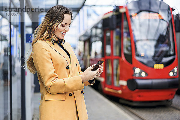 Frau schickt SMS über ihr Smartphone  während sie an der Straßenbahnhaltestelle wartet