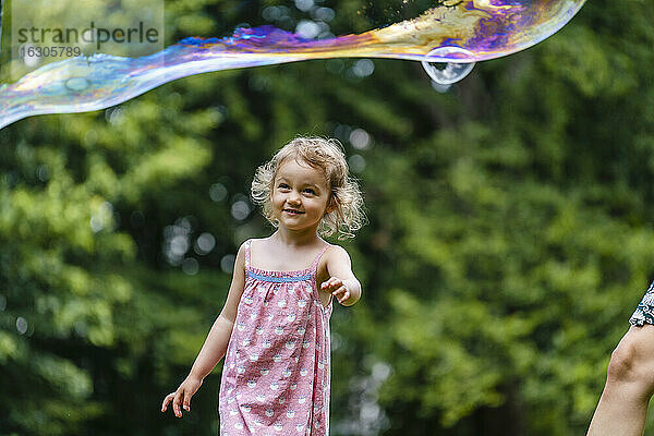 Lächelndes Mädchen  das eine Blase betrachtet  während es im Park steht
