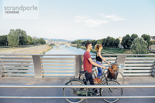 Paar mit Fahrrädern zu Fuß auf Brücke über Fluss gegen Himmel